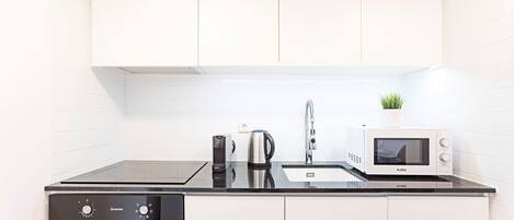 A modern kitchen with white cabinets, a black countertop, a microwave, a kettle, and a coffee maker.
