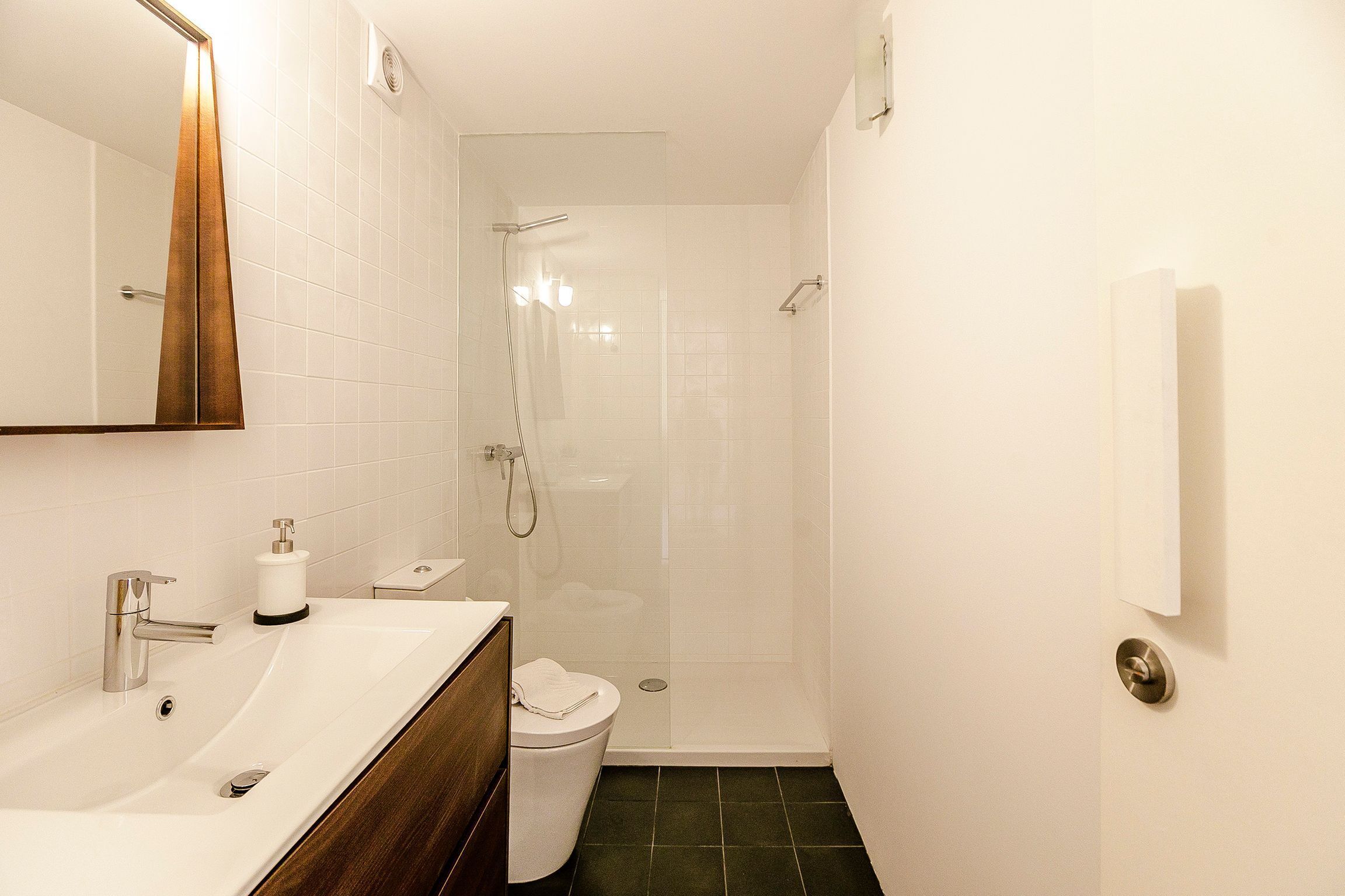 A modern bathroom with a large mirror, a sink, a toilet, and a glass-enclosed shower.