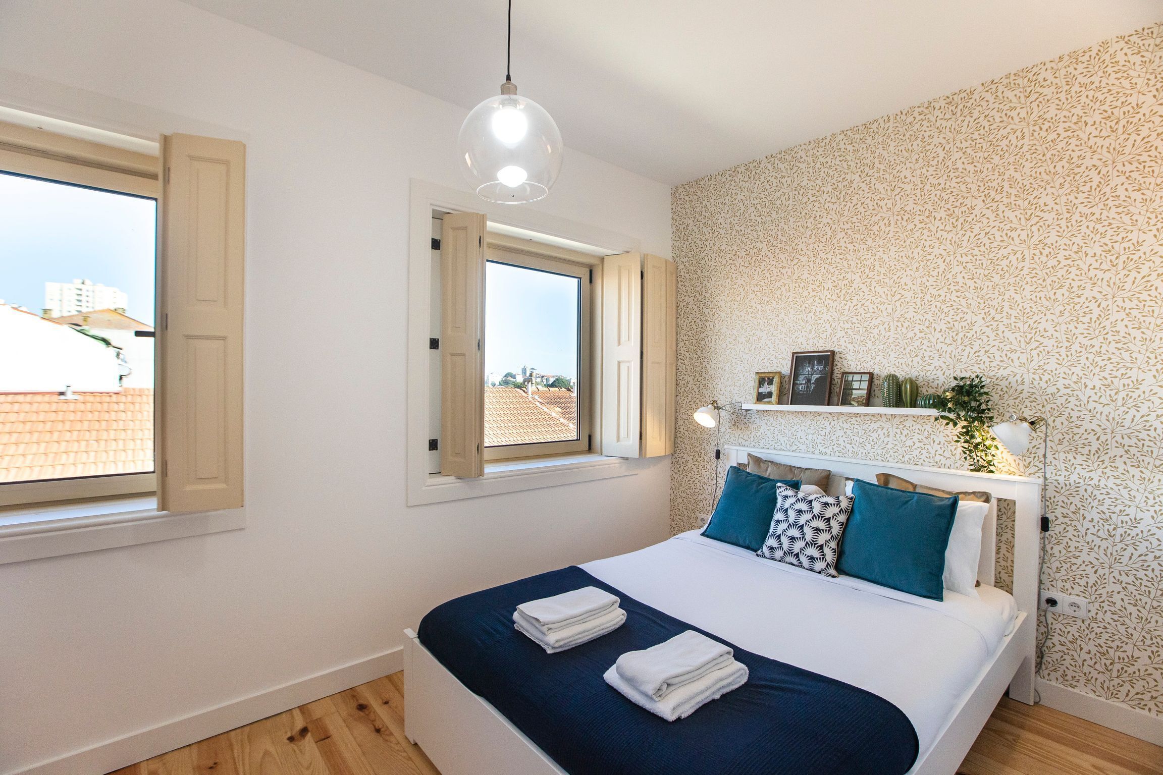 A bedroom with a bed, two windows, a headboard with a shelf, and a patterned wall.