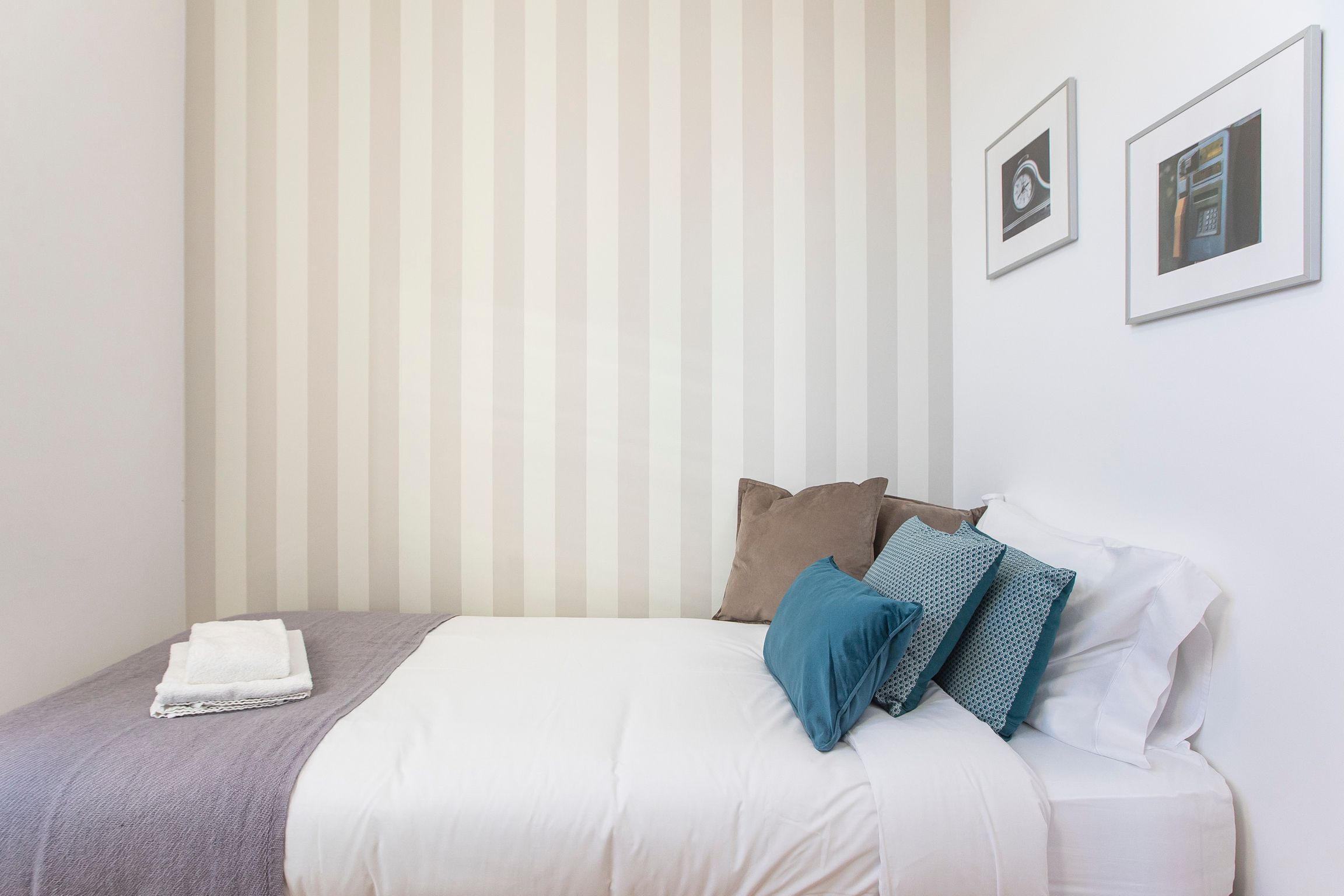 A neatly made bed with white and grey bedding, a grey blanket, and multiple pillows in various colors.