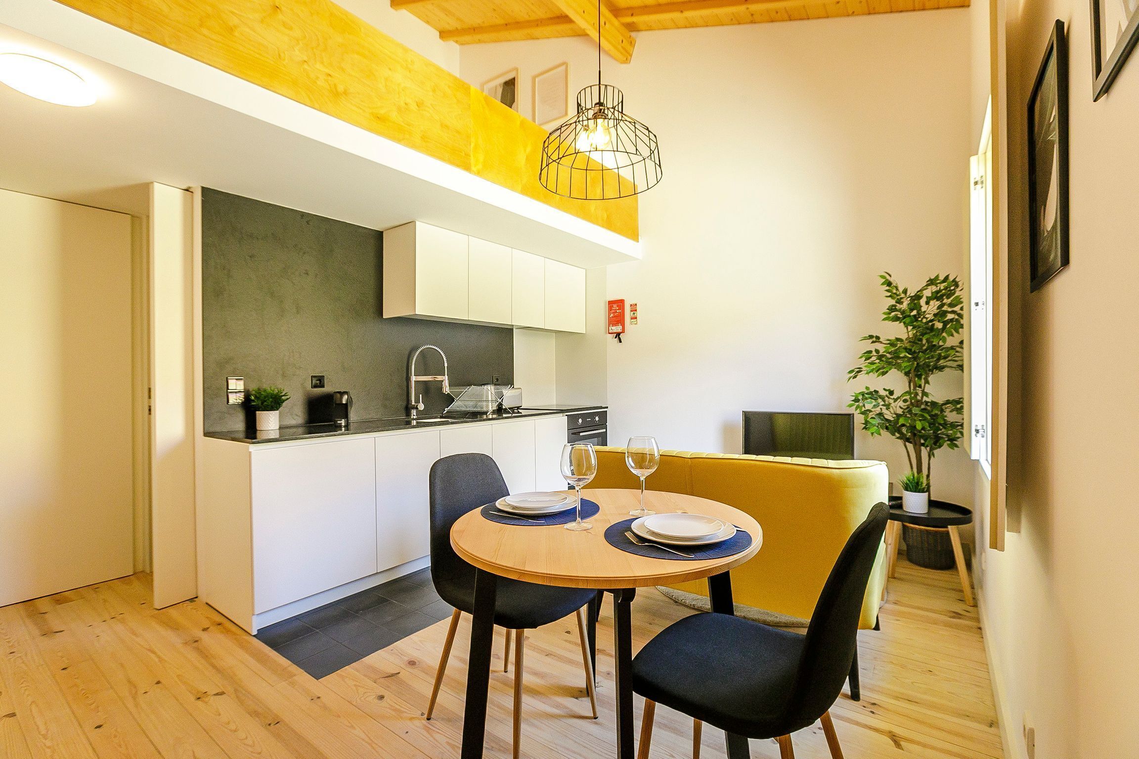 Une cuisine de taille réduite avec des meubles blancs, une table à manger avec deux chaises et un canapé jaune.