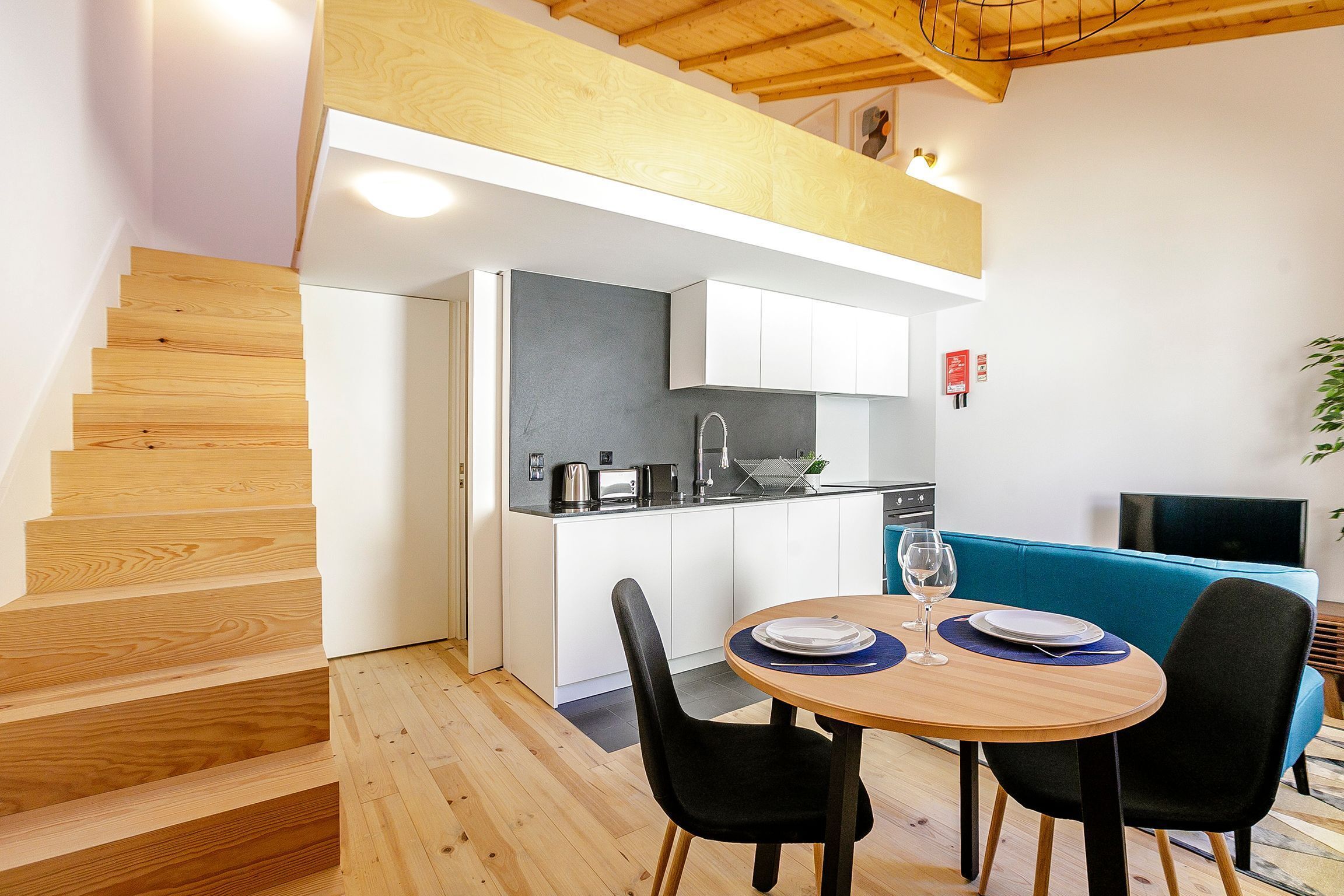 Een moderne keuken met witte kastjes, een zwart aanrecht en een eethoek met een ronde houten tafel en zwarte stoelen.