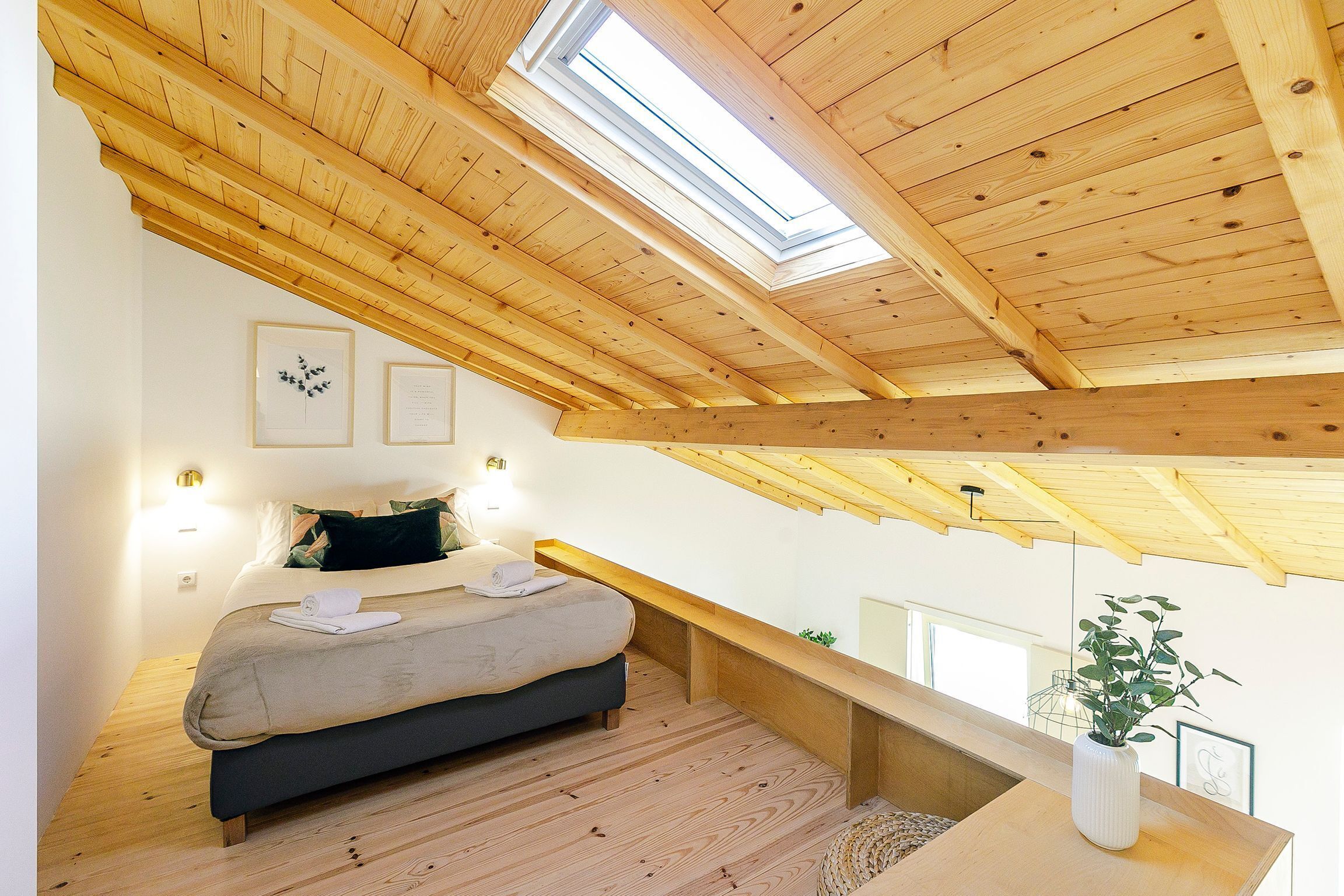 A bedroom with a skylight, a bed, a bedside table, and a plant.