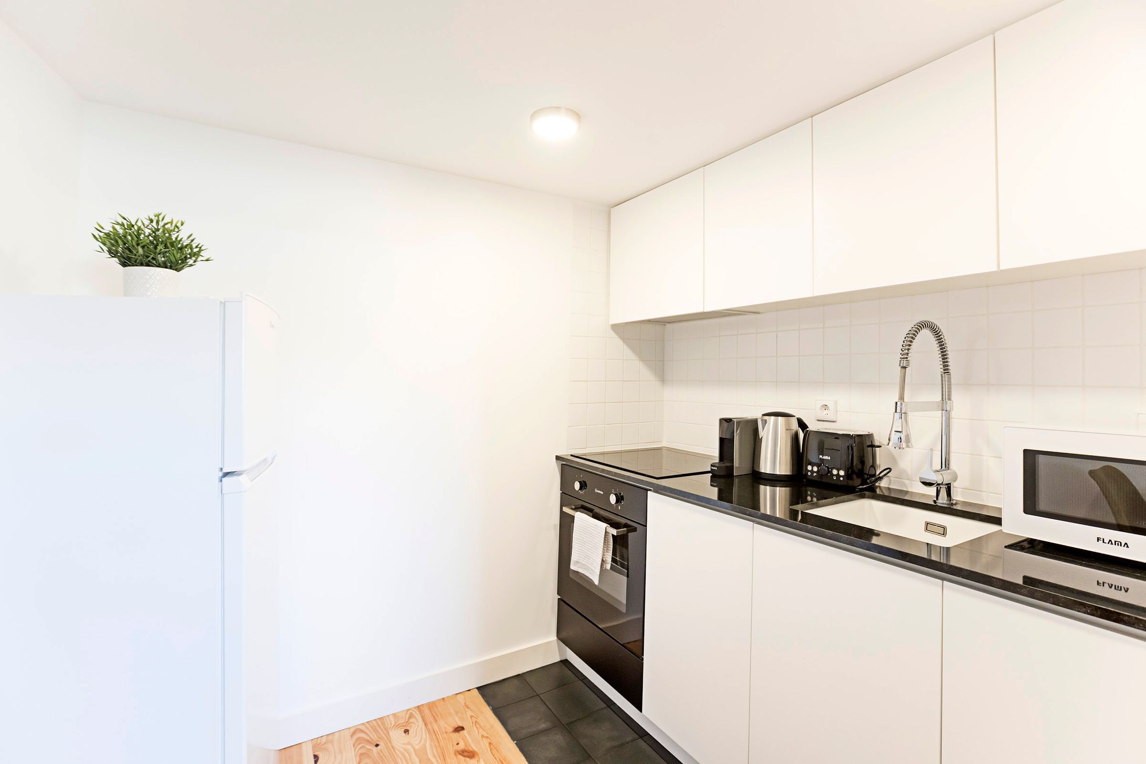 A modern kitchen with white cabinets, a black countertop, a stainless steel sink, and a built-in oven.