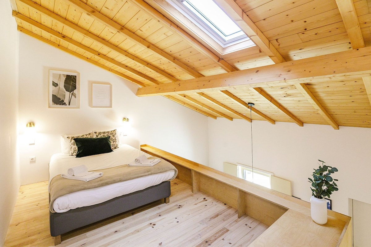 A bedroom with a skylight, wooden beams, a bed, a bedside table, and a potted plant.