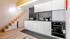 Eine moderne Küche mit weißen Schränken, einem eingebauten Backofen und einer Holztreppe.