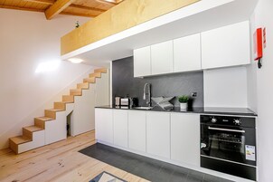 A modern kitchen with white cabinets, a built-in oven, and a wooden staircase.