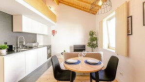 Eine moderne Küche mit weißen Schränken, einer Holzbalkendecke und einem Essbereich mit rundem Tisch und schwarzen Stühlen.