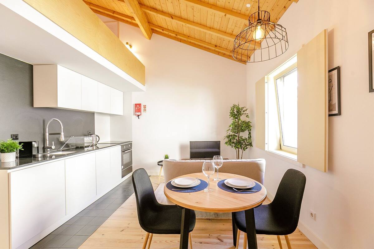 A modern kitchen with white cabinets, a wooden ceiling, and a dining area with a round table and black chairs.