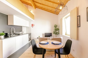 A modern kitchen with white cabinets, a wooden ceiling, and a dining area with a round table and black chairs.