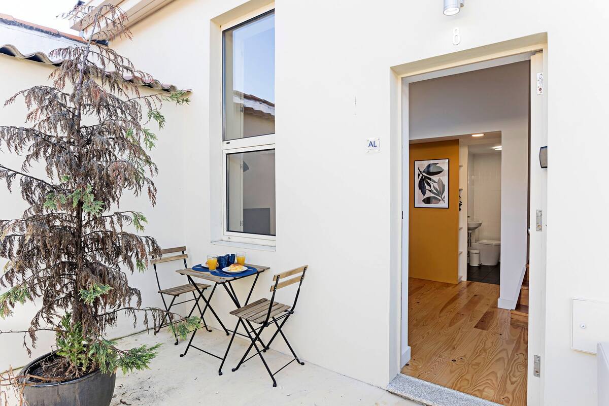 A small patio with a table and chairs, a potted plant, and a door leading to an interior space.