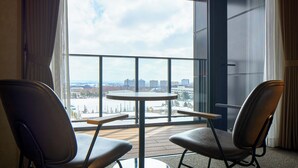 Een balkon met twee stoelen en een kleine tafel, met uitzicht op een stadsbeeld met gebouwen en een met sneeuw bedekte grond.