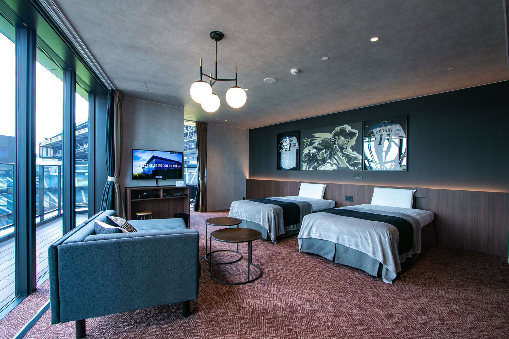 Quarto de hotel moderno com duas camas, um sofá, uma TV e uma janela grande com vista para a cidade.