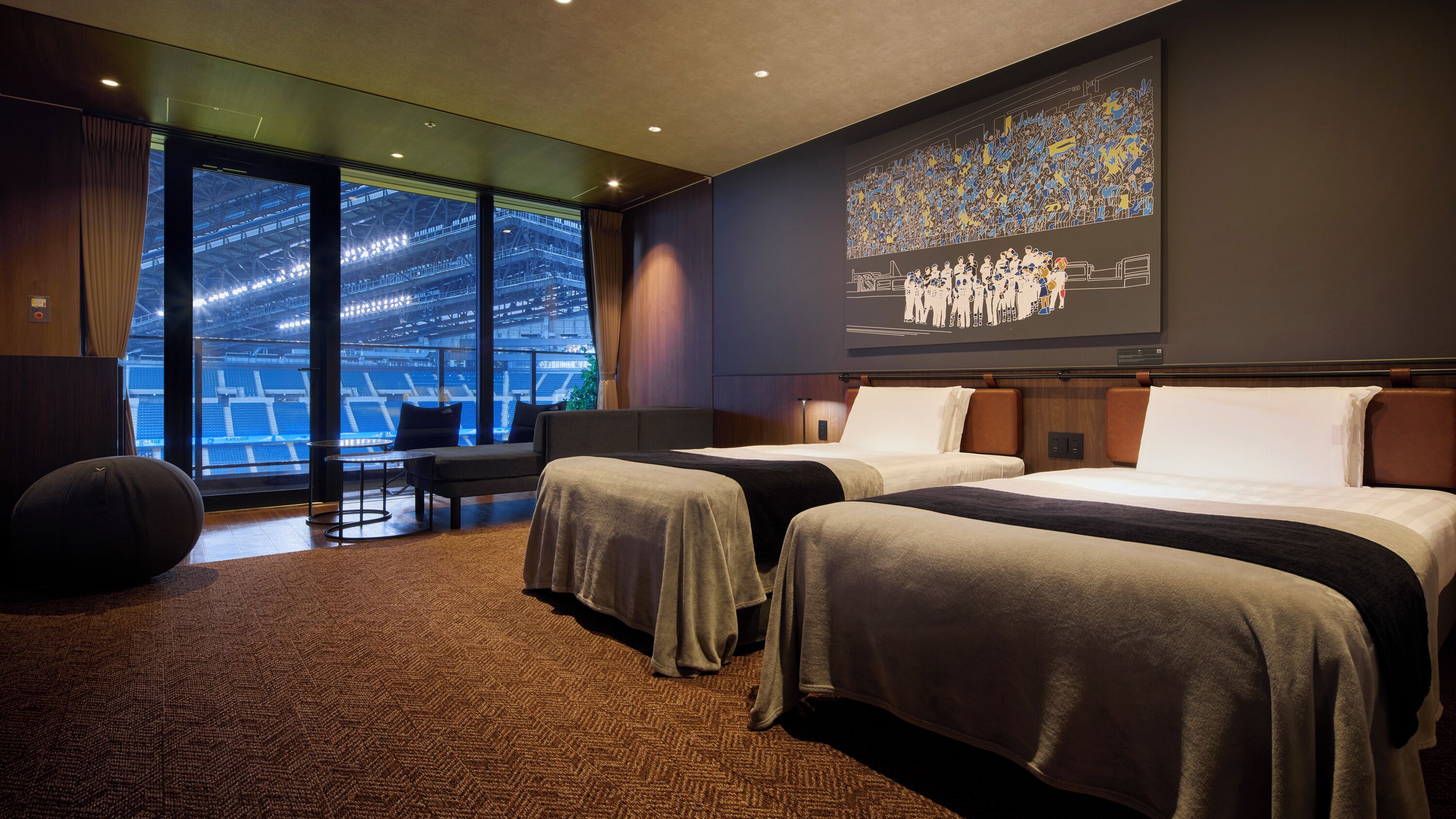 A hotel room with two beds, a large window with a view of a stadium, and a mural on the wall.