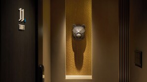 Een gang met een beeldhouwwerk van een berenhoofd, een deur met een bordje en een gestructureerde wand.