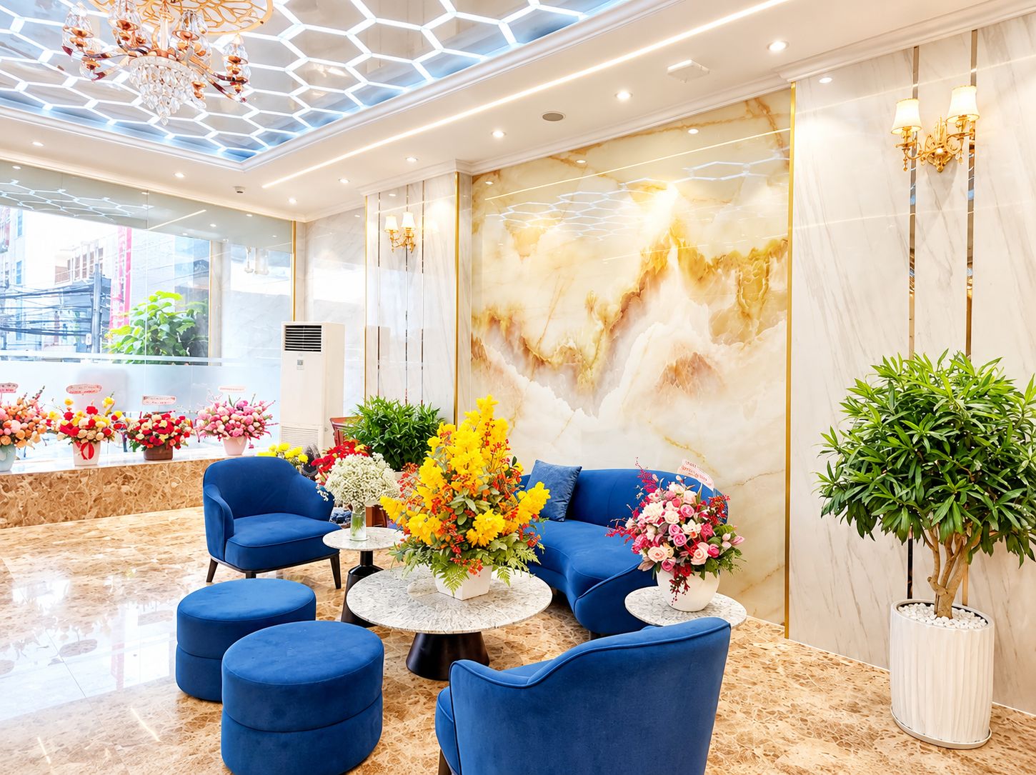 Un vestíbulo moderno con piso de mármol, asientos azules y un gran arreglo floral.