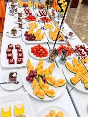 Una mesa de buffet con diversos alimentos, incluyendo postres, frutas y verduras.