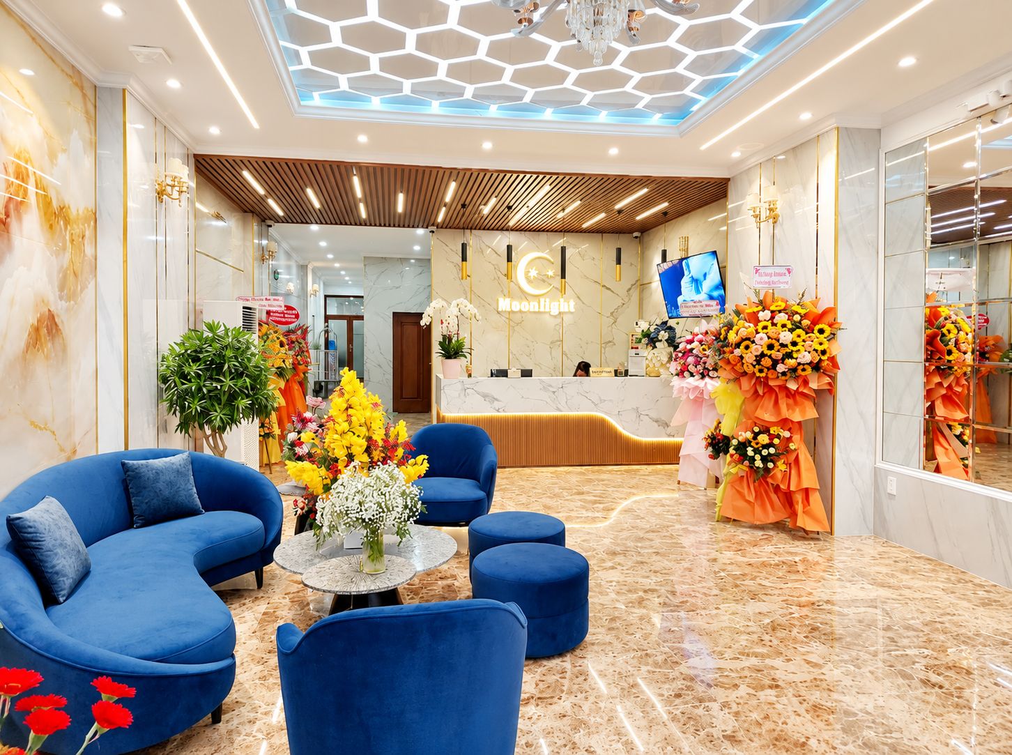 Un vestíbulo de hotel con mostrador de recepción, zona de estar azul y arreglos florales.
