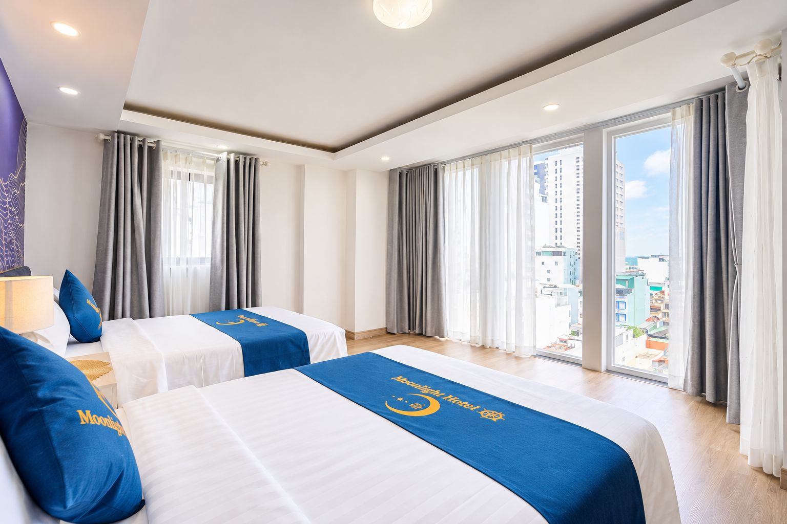 A hotel room with two beds, a city view, and a large window with curtains.