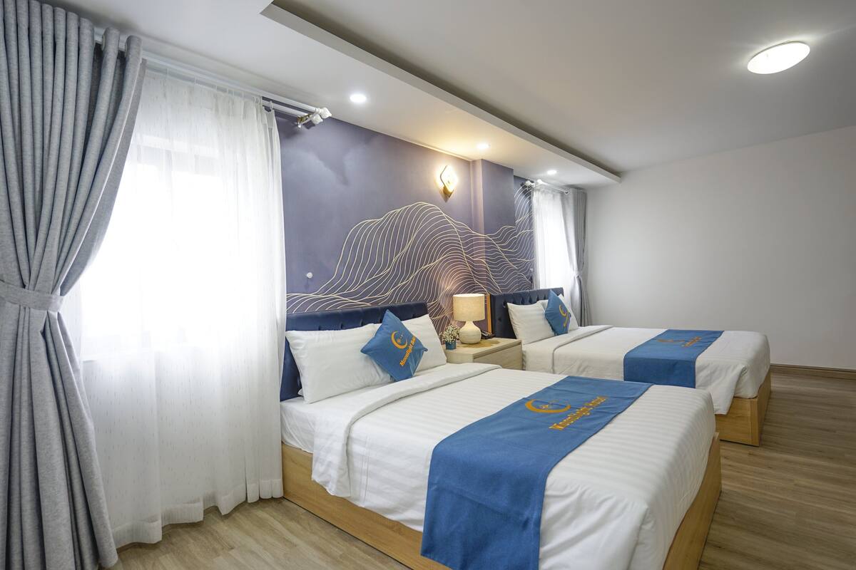 Ein Hotelzimmer mit zwei Betten, einem großen Fenster mit Vorhängen, einer Wandlampe und einem Wandbild.