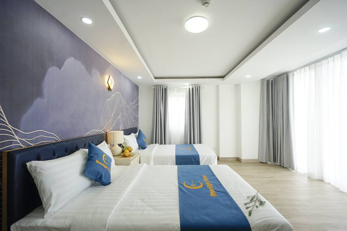 Ein Hotelzimmer mit zwei Betten, einem Nachttisch, einer Wandlampe und einem großen Fenster mit Vorhängen.