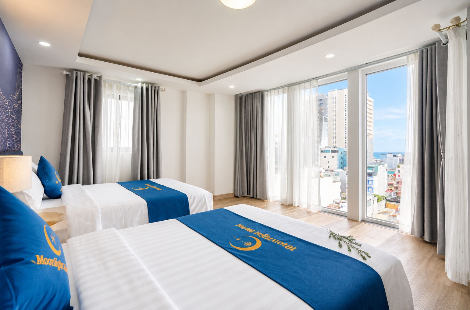 Habitación de hotel con dos camas, un ventanal con cortinas y vista a la ciudad.