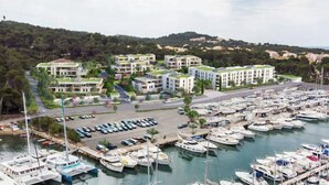 Ein Yachthafen mit mehreren dort vertäuten Booten, einem Parkplatz und einem Wohnkomplex mit moderner Architektur und begrünten Dächern.