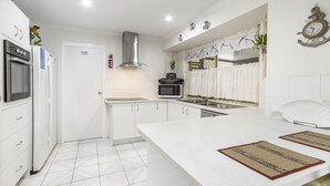 A modern kitchen with white cabinetry, a stainless steel range hood, a microwave, and a sink.