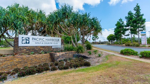 A sign for Pacific Harbour Golf & Country Club with a landscaped area and trees.