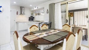 A dining area with a round table, six chairs, and a kitchen in the background.