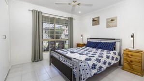 A bedroom with a bed, a nightstand, a bedside lamp, a ceiling fan, and a window with blinds.