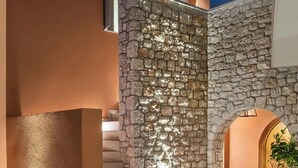 Un edificio moderno con fachada de piedra, una escalera de madera y un pequeño árbol en una jardinera.