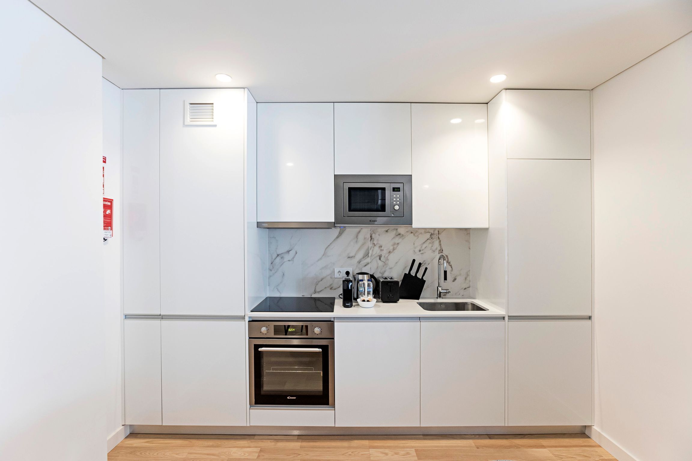 A compact kitchen with white cabinets, a built-in microwave, a stove, and a sink.