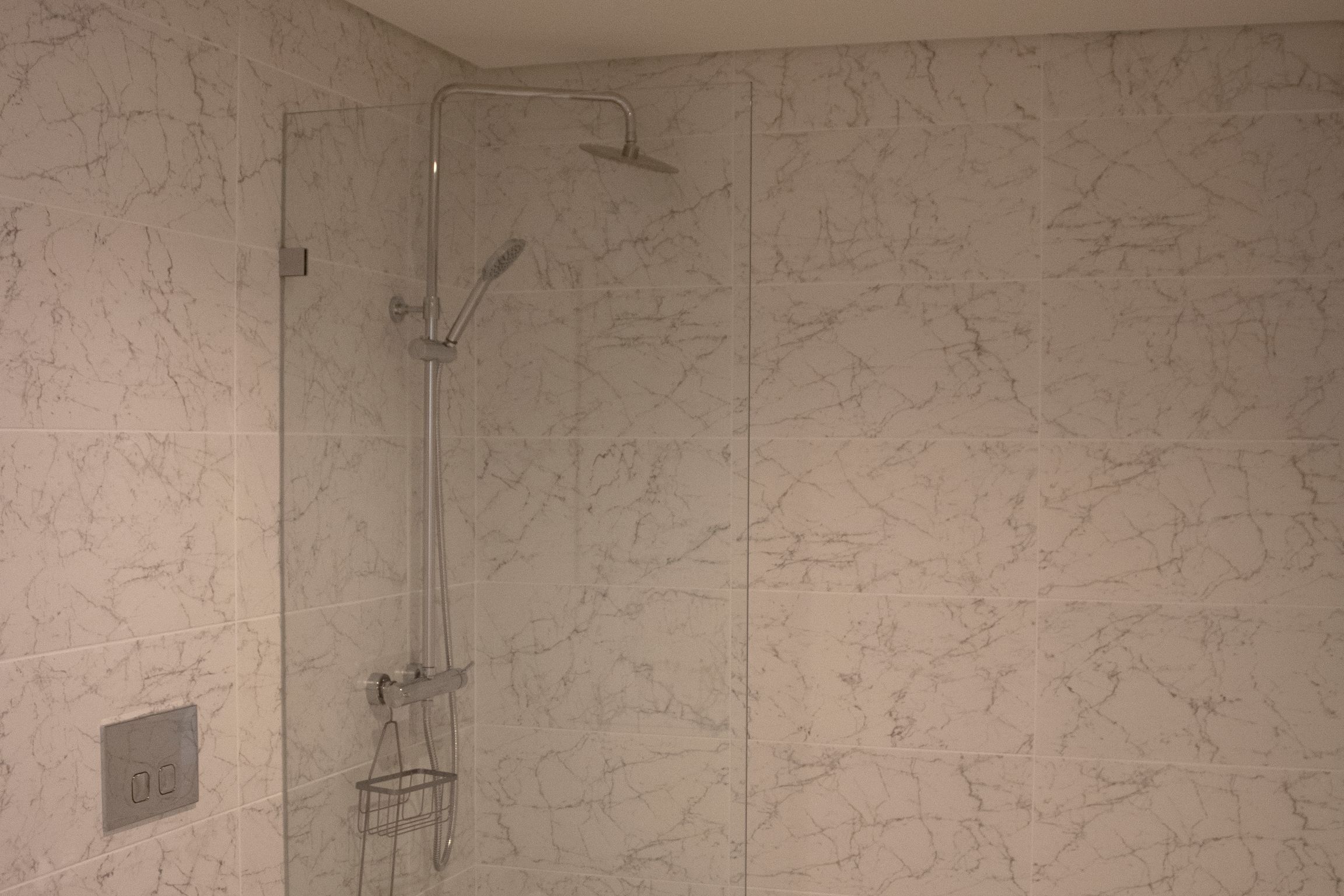A shower with a handheld showerhead and a wall-mounted faucet, set against a marble-patterned wall.