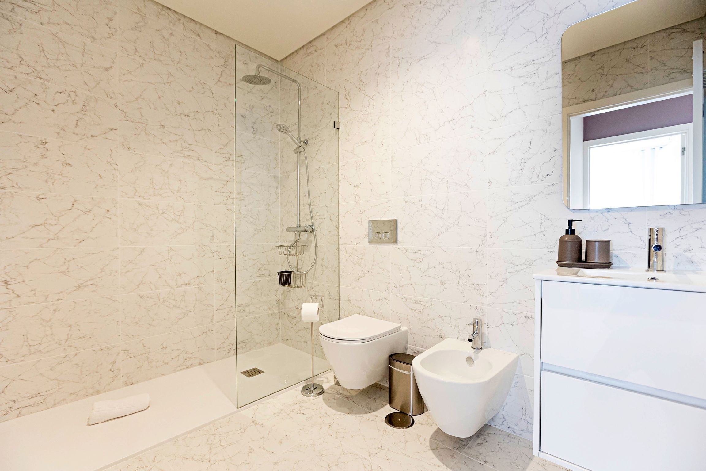 Ein modernes Badezimmer mit Duschkabine aus Glas, Toilette, Bidet und Waschtisch mit Spiegel.
