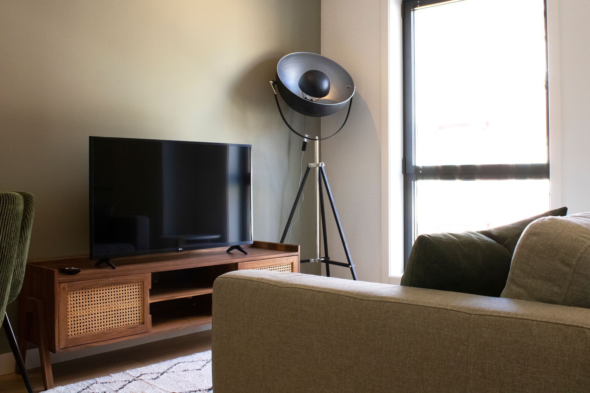 A living room with a flat-screen TV on a wooden stand, a floor lamp, and a sofa.