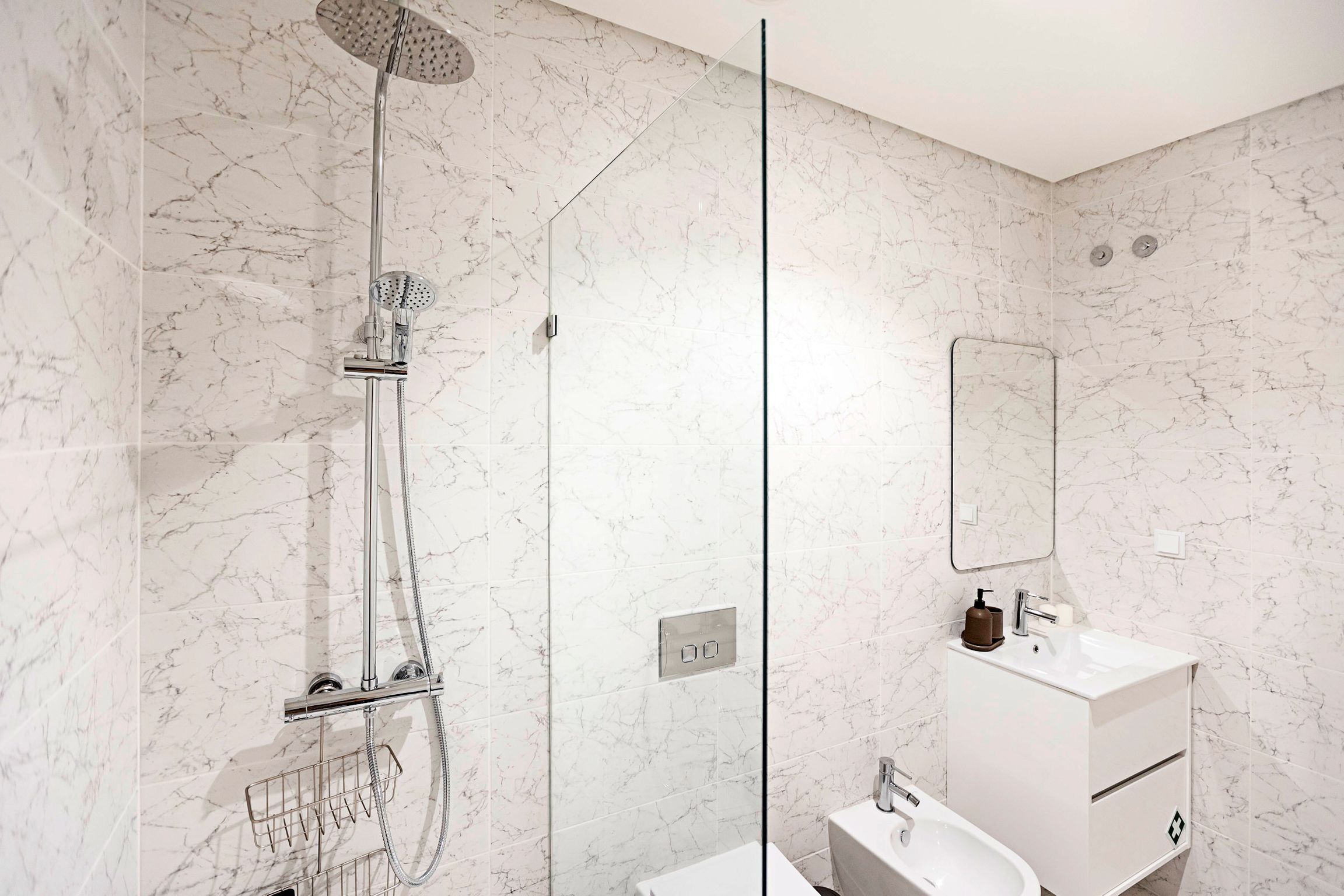A modern bathroom with a glass-enclosed shower, a white sink, and a marble-tiled wall.