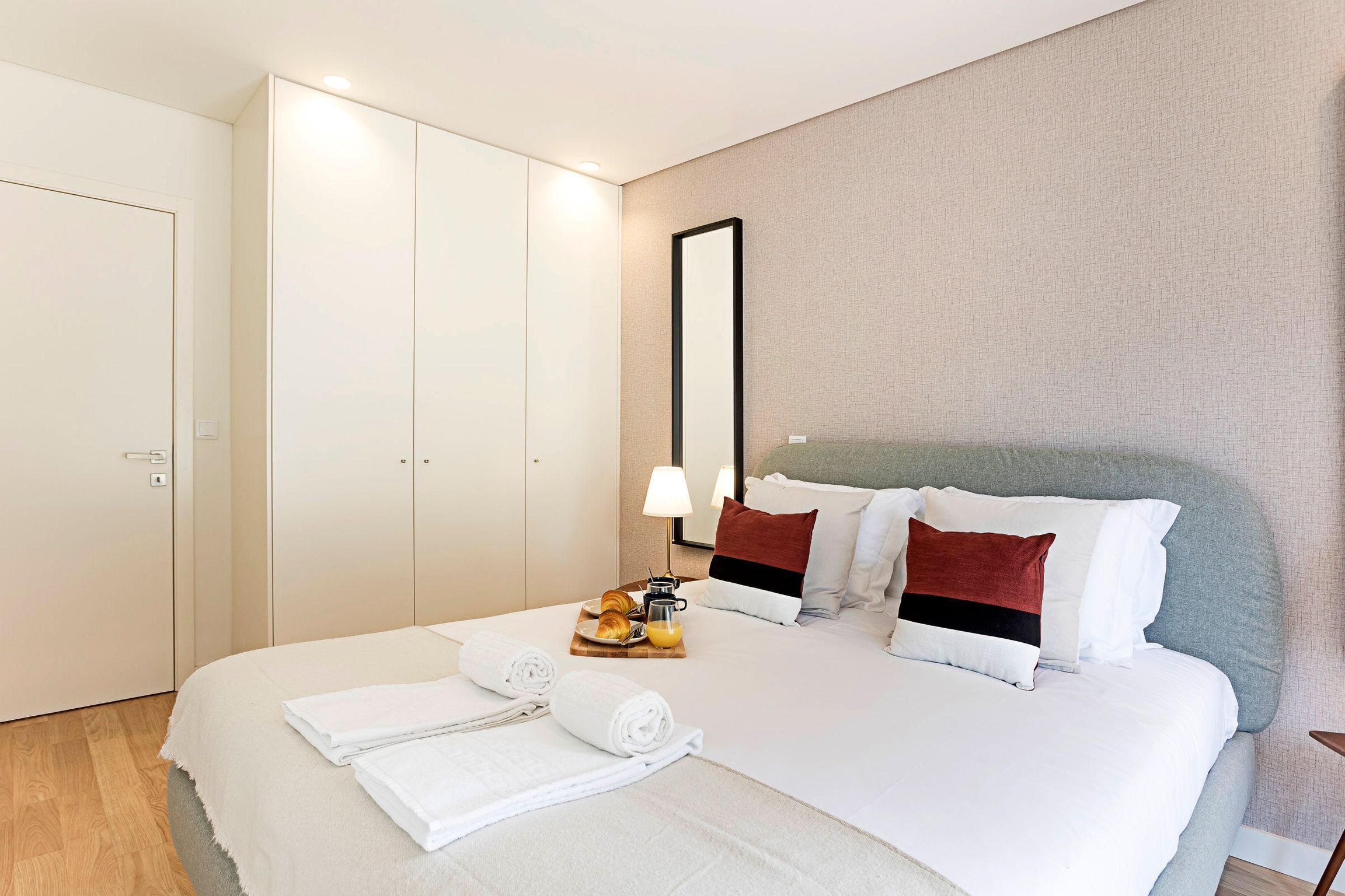 A hotel room with a large bed, a bedside table with a lamp, and a tray of breakfast items.