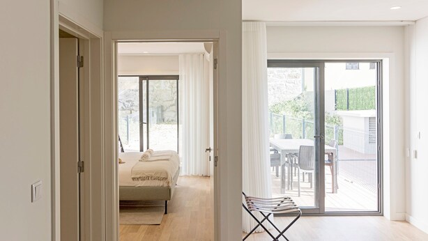 A modern bedroom with a bed, a balcony with a table and chairs, and a sliding glass door leading to an outdoor area. - Rua do Paraíso (Porto)