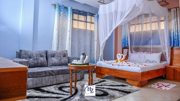 A hotel room with a bed, a sofa, a small table, and a window with curtains. - Hotel Zesper (Kisii)