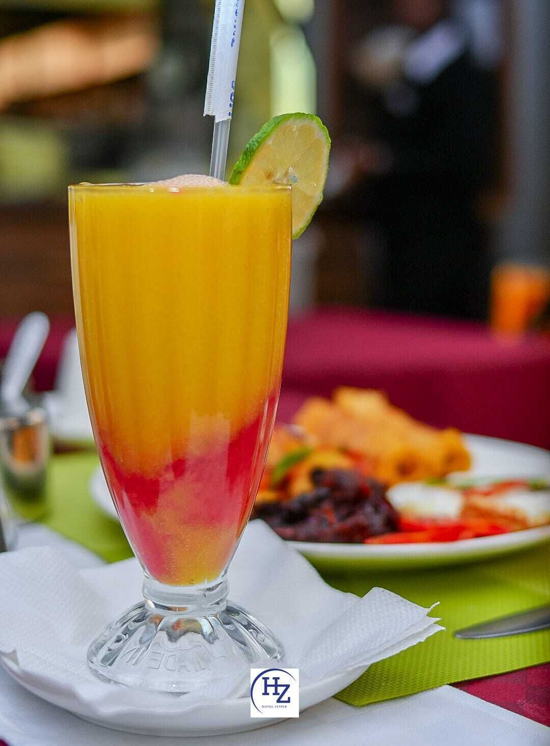 A tall glass of layered fruit juice with a lime wedge, placed on a white napkin.