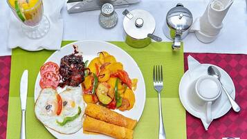 Un plato de desayuno con huevos, verduras y carne, una taza de café y una tetera sobre una mesa con un mantel individual.