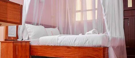A bedroom with a wooden bed, white bedding, a wooden nightstand, a bedside table, and a wooden wardrobe.