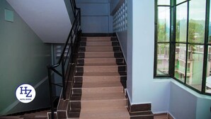 A staircase with a handrail, leading to a landing with a large window offering a view of buildings and greenery. - Hotel Zesper (Kisii)