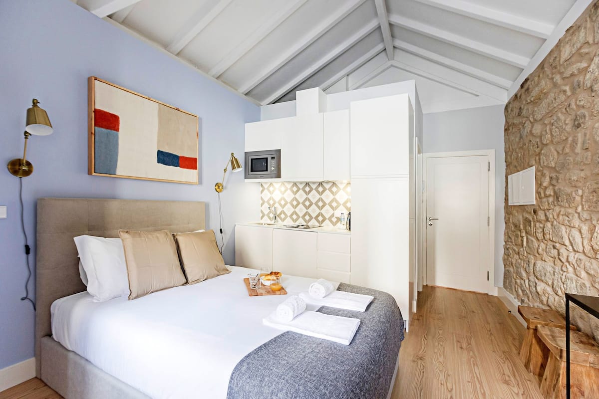 A bedroom with a bed, a nightstand, a lamp, a microwave, and a stone wall.