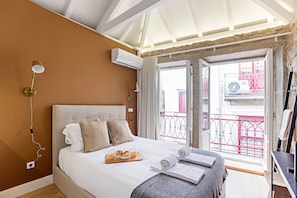 A hotel room with a bed, breakfast tray, towels, and an air conditioning unit.