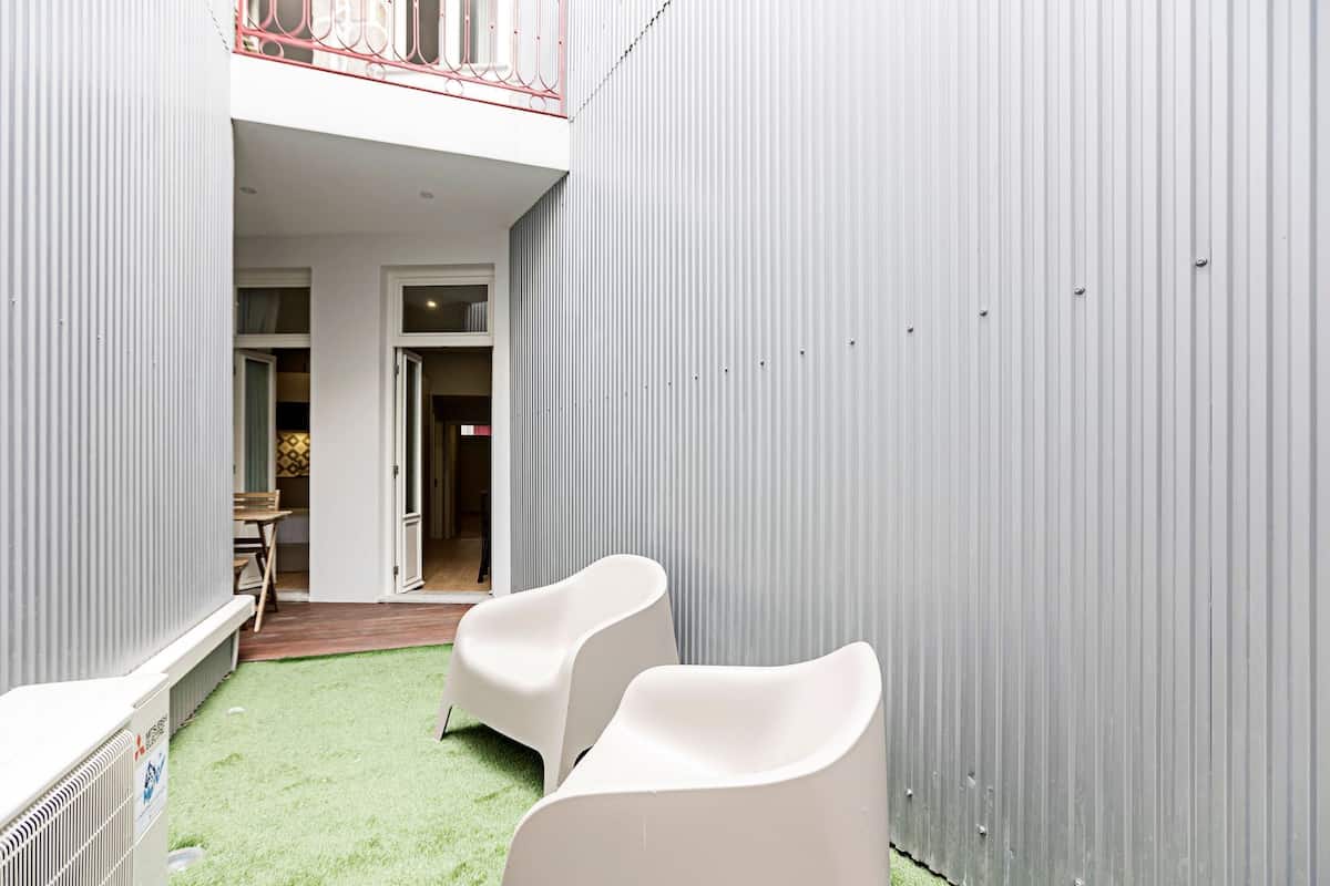 A compact outdoor area with two white chairs, a small table, and a door leading to an interior space.