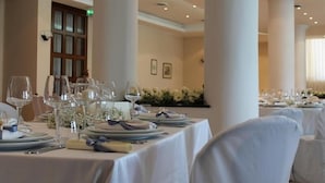 Een balzaal met gedekte tafels voor een formeel evenement, met witte tafelkleden, servies en bloemdecoraties.