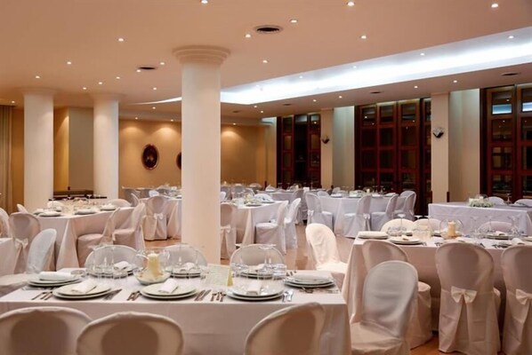 A banquet hall with round tables set for dining, white chairs, and a high ceiling with recessed lighting. - Hotel Serenella (Agropoli)