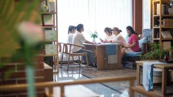 Un grupo de personas sentadas alrededor de una mesa en una habitación con una estantería y una planta.